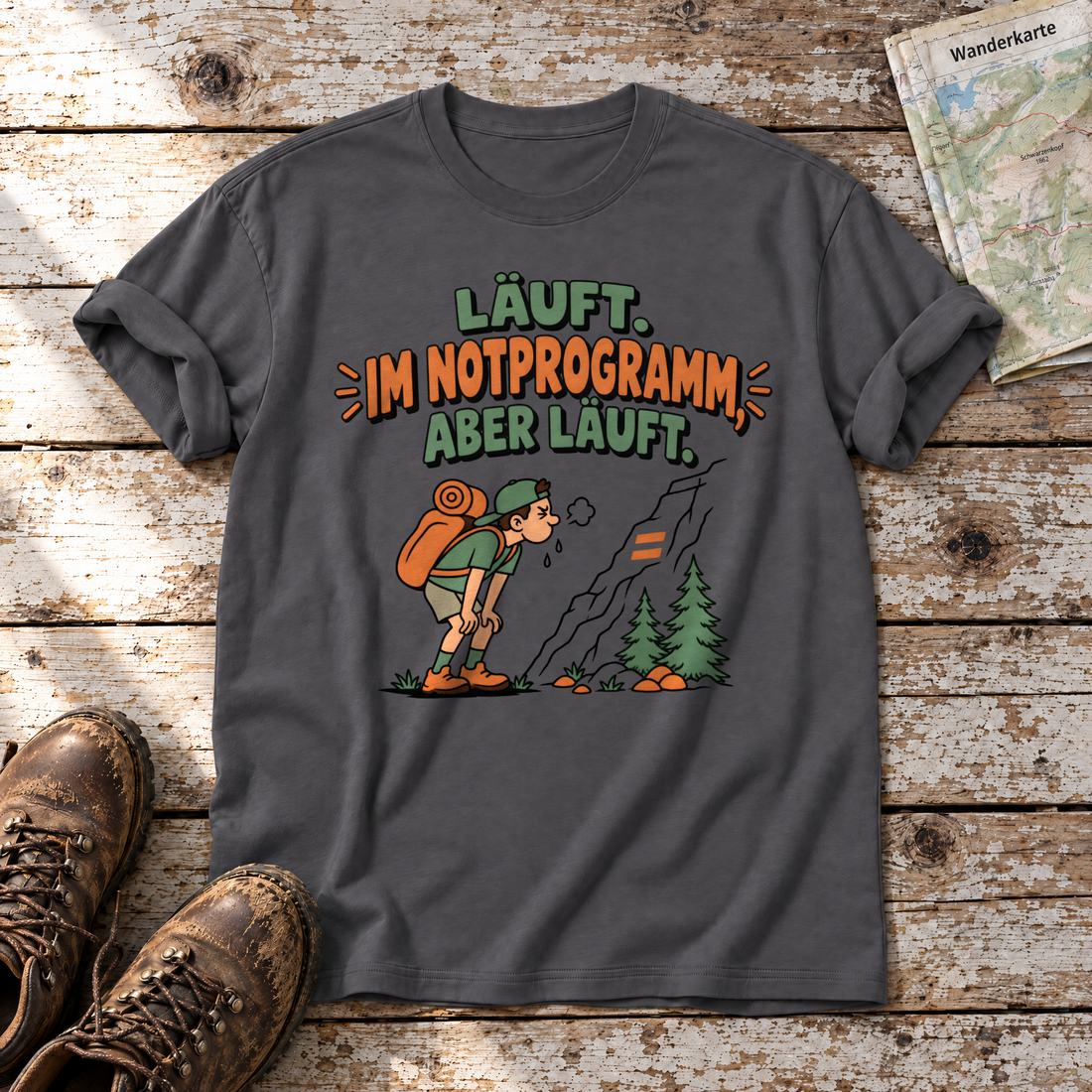 Im Notprogramm, aber läuft – T-Shirt Unisex in Dunkelgrau, flach liegend auf alten Holzbrettern mit Wanderschuhen und Wanderkarte.