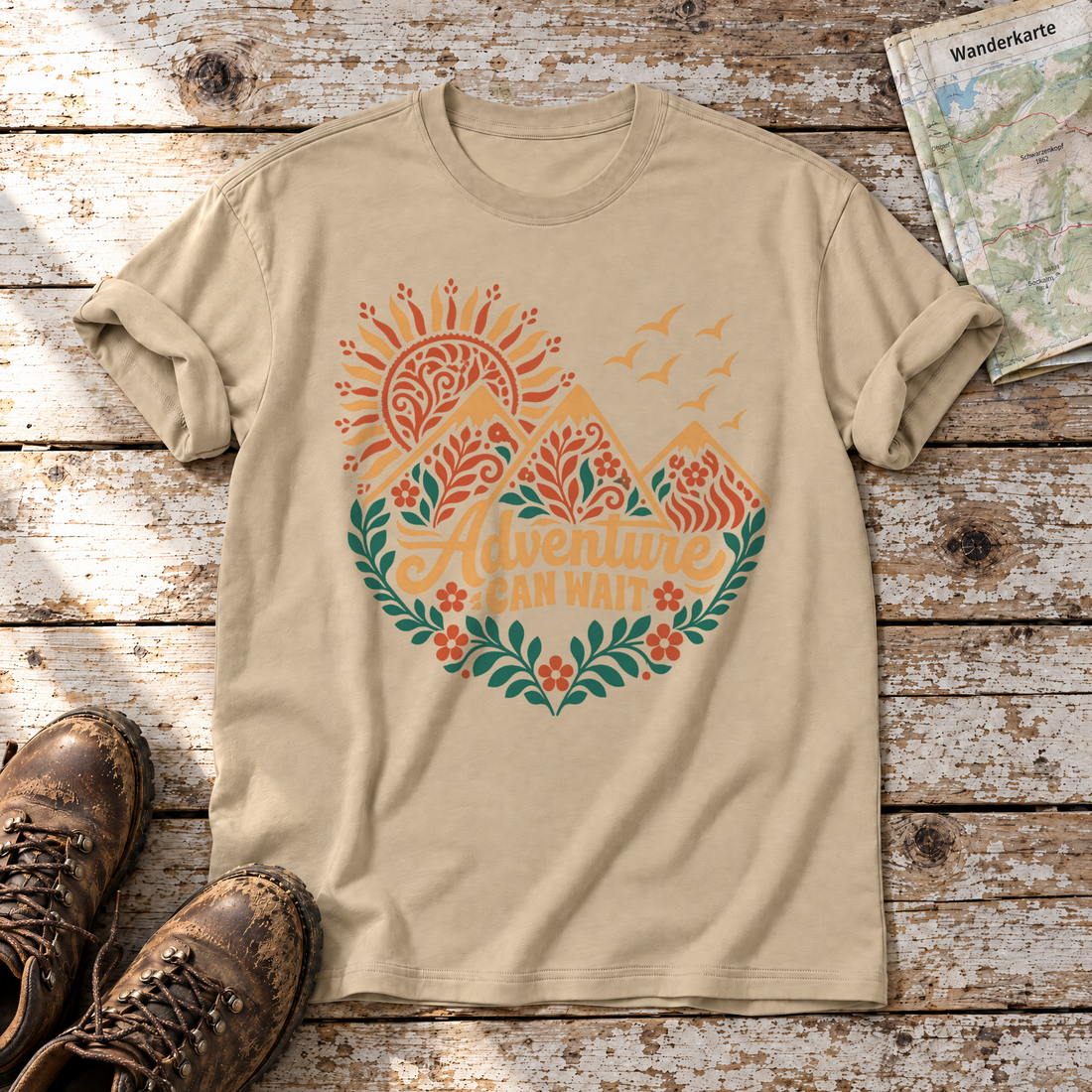 Adventure can wait – T-Shirt Unisex in Sand, flach liegend auf alten Holzbrettern mit Wanderschuhen und Wanderkarte.