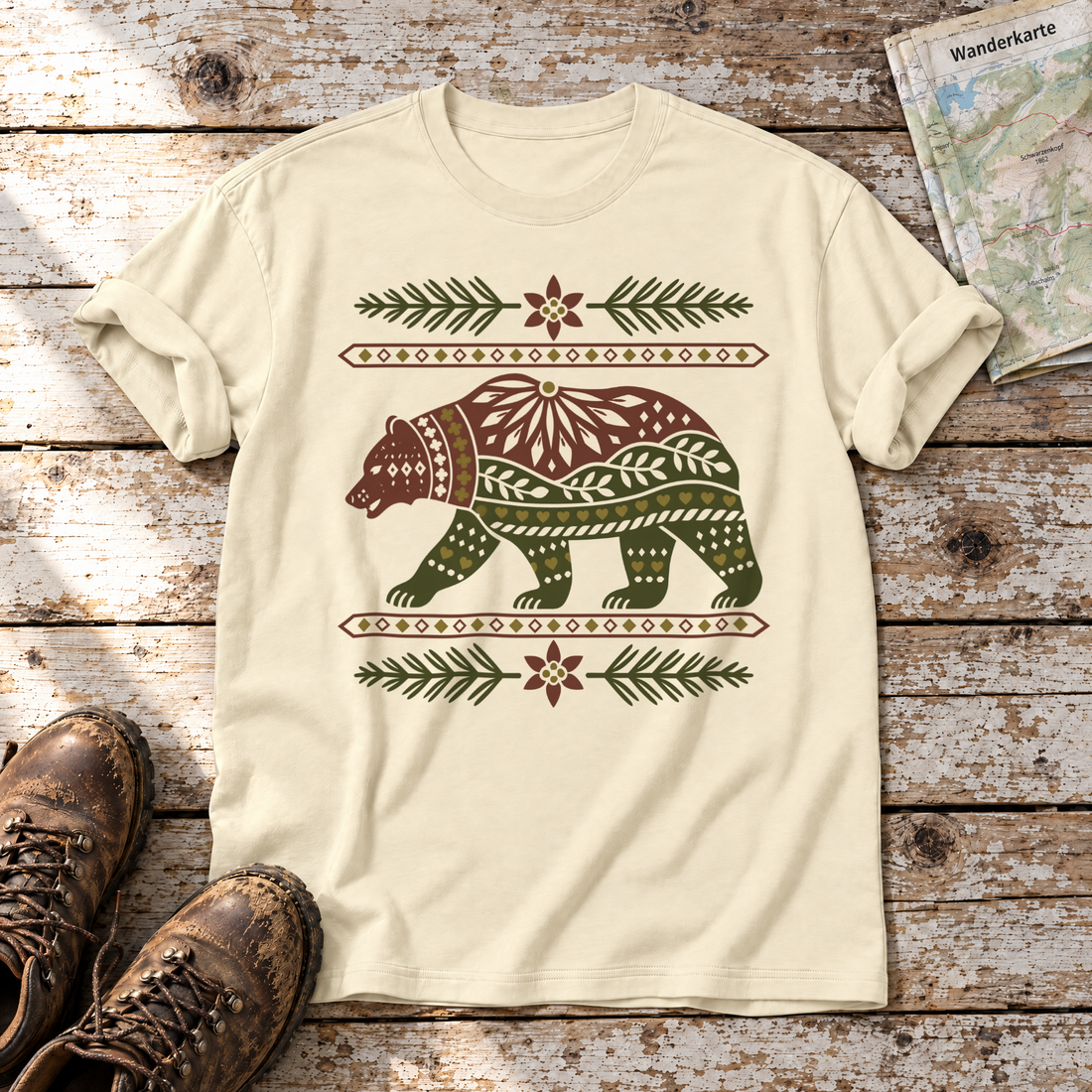 Bär im Alpenornament – T-Shirt Unisex in Natur, flach liegend auf alten Holzbrettern mit Wanderschuhen und Wanderkarte.