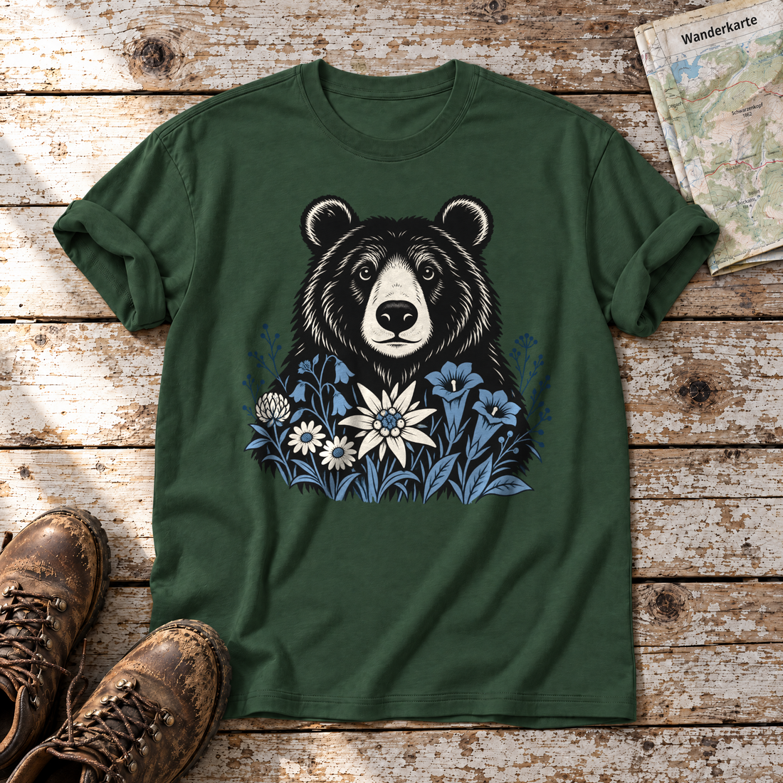 Bär in der Alpenwiese – T-Shirt Unisex in Flaschengrün, flach liegend auf alten Holzbrettern mit Wanderschuhen und Wanderkarte.