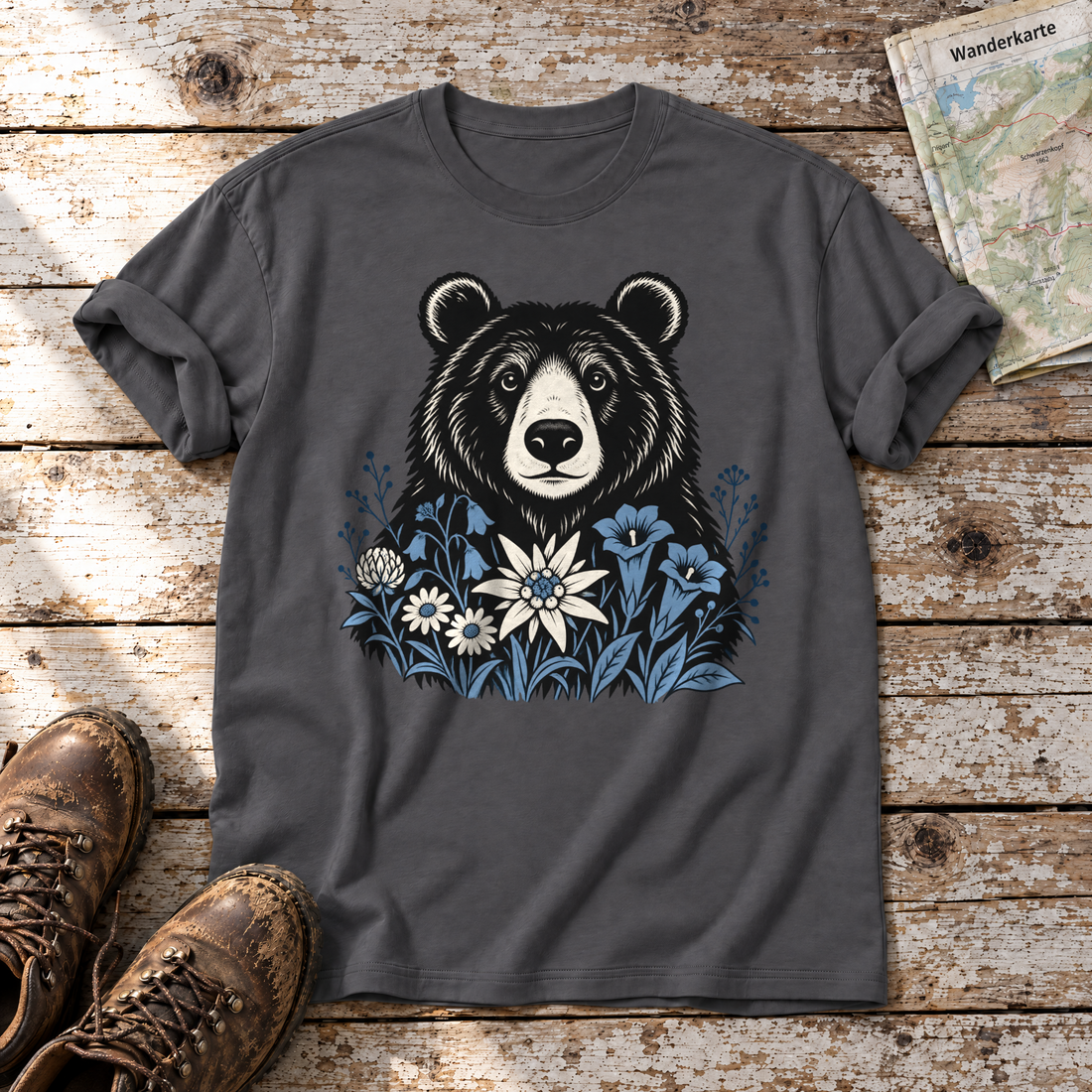 Bär in der Alpenwiese – T-Shirt Unisex in Dunkelgrau, flach liegend auf alten Holzbrettern mit Wanderschuhen und Wanderkarte.