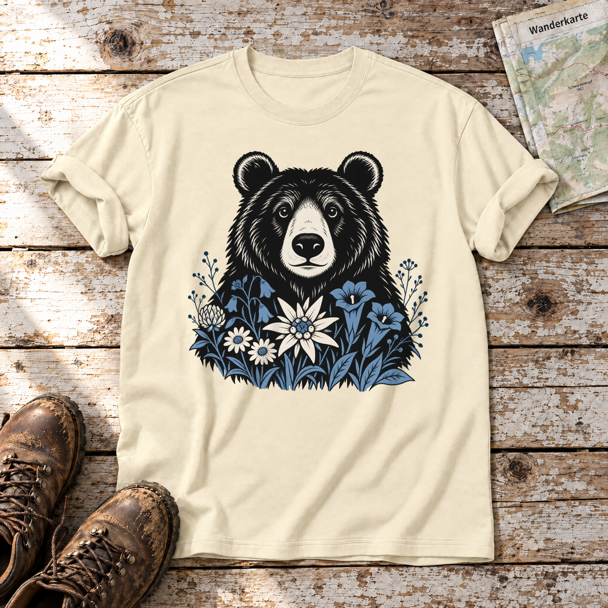 Bär in der Alpenwiese – T-Shirt Unisex in Natur, flach liegend auf alten Holzbrettern mit Wanderschuhen und Wanderkarte.