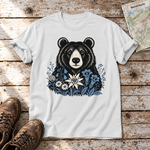 Bär in der Alpenwiese – T-Shirt Unisex in Weiß, flach liegend auf alten Holzbrettern mit Wanderschuhen und Wanderkarte.