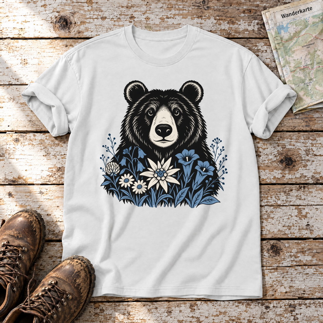 Bär in der Alpenwiese – T-Shirt Unisex in Weiß, flach liegend auf alten Holzbrettern mit Wanderschuhen und Wanderkarte.