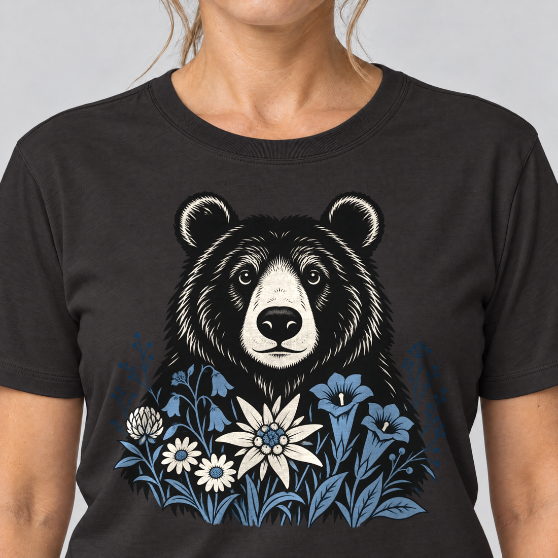 Nahaufnahme des Drucks: Bär in der Alpenwiese – T-Shirt Unisex in Schwarz, von einer Frau getragen
