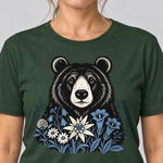 Nahaufnahme des Drucks: Bär in der Alpenwiese – T-Shirt Unisex in Flaschengrün, von einer Frau getragen