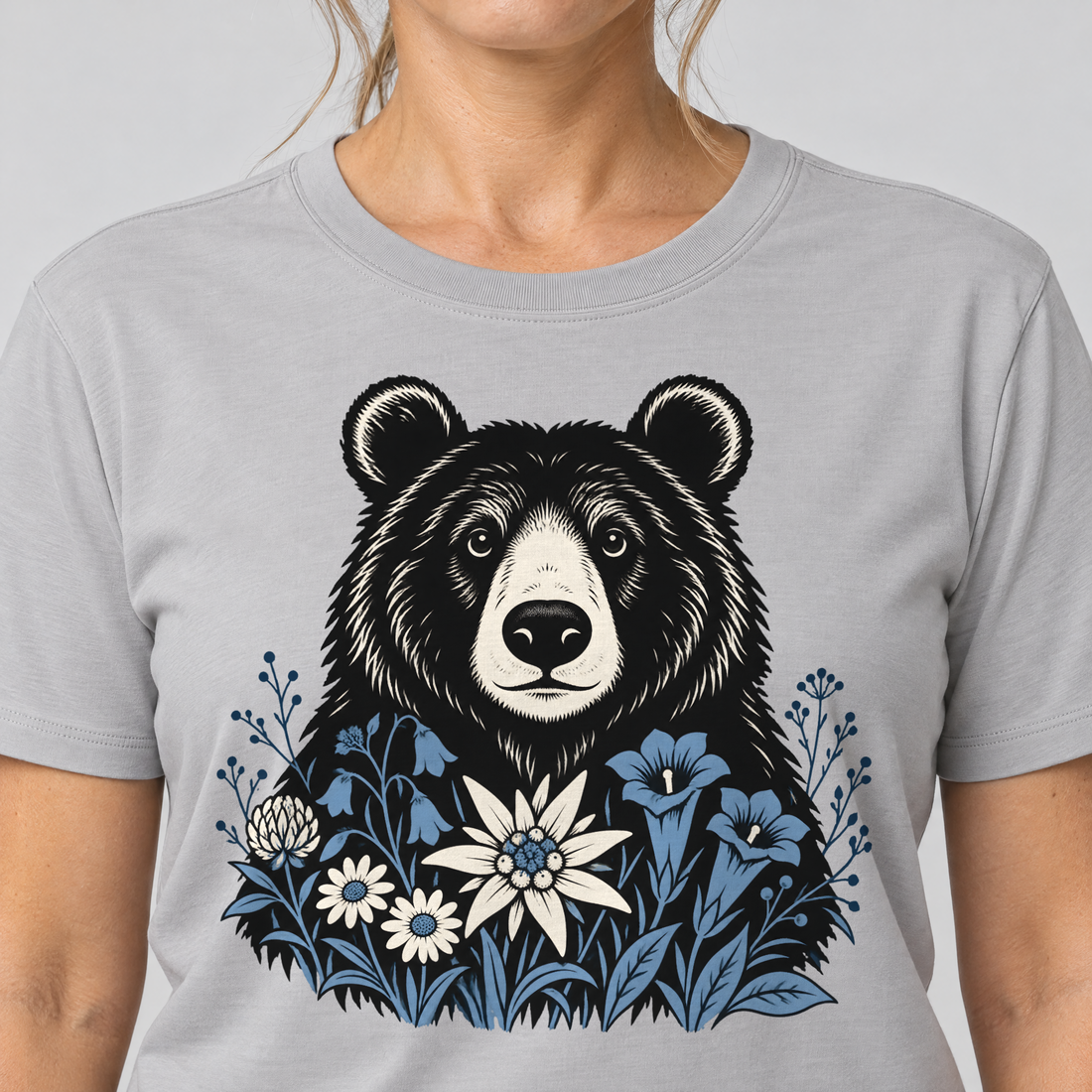 Nahaufnahme des Drucks: Bär in der Alpenwiese – T-Shirt Unisex in Hellgrau, von einer Frau getragen