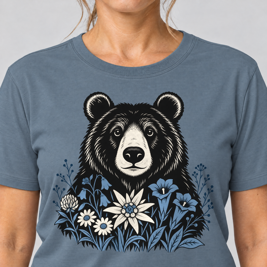 Nahaufnahme des Drucks: Bär in der Alpenwiese – T-Shirt Unisex in Steinblau, von einer Frau getragen