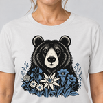 Nahaufnahme des Drucks: Bär in der Alpenwiese – T-Shirt Unisex in Weiß, von einer Frau getragen