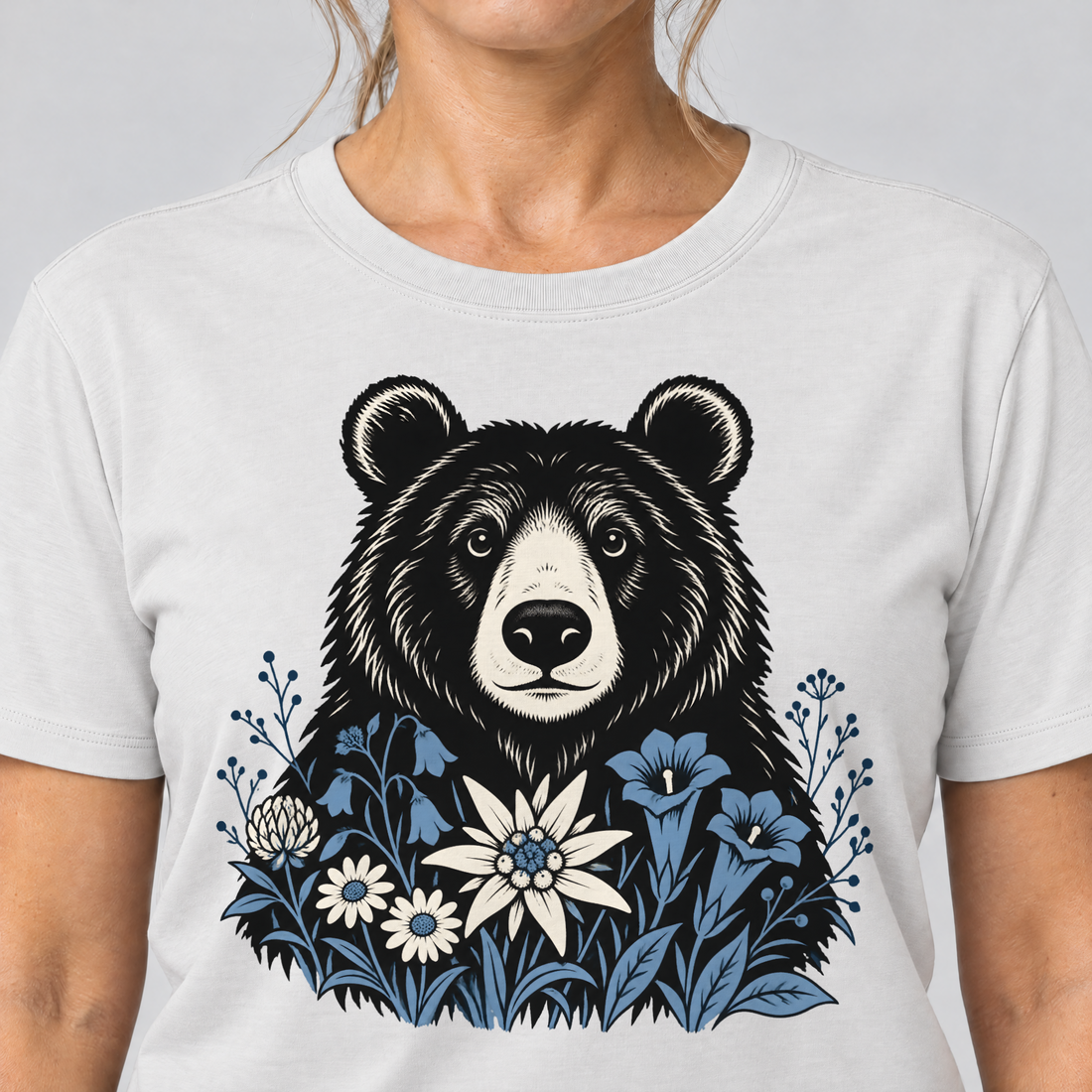 Nahaufnahme des Drucks: Bär in der Alpenwiese – T-Shirt Unisex in Weiß, von einer Frau getragen