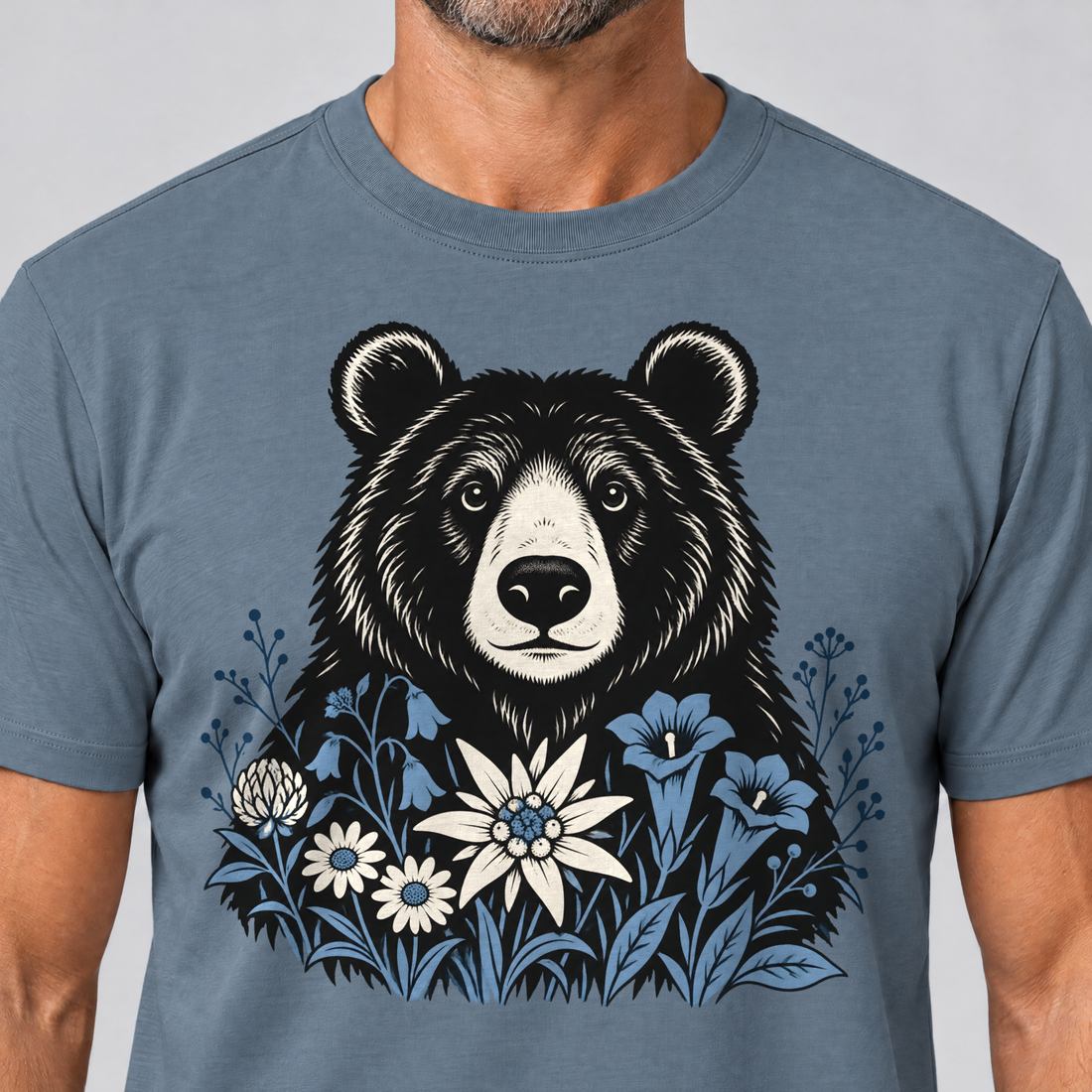 Nahaufnahme des Drucks: Bär in der Alpenwiese – T-Shirt Unisex in Steinblau, von einem Mann getragen