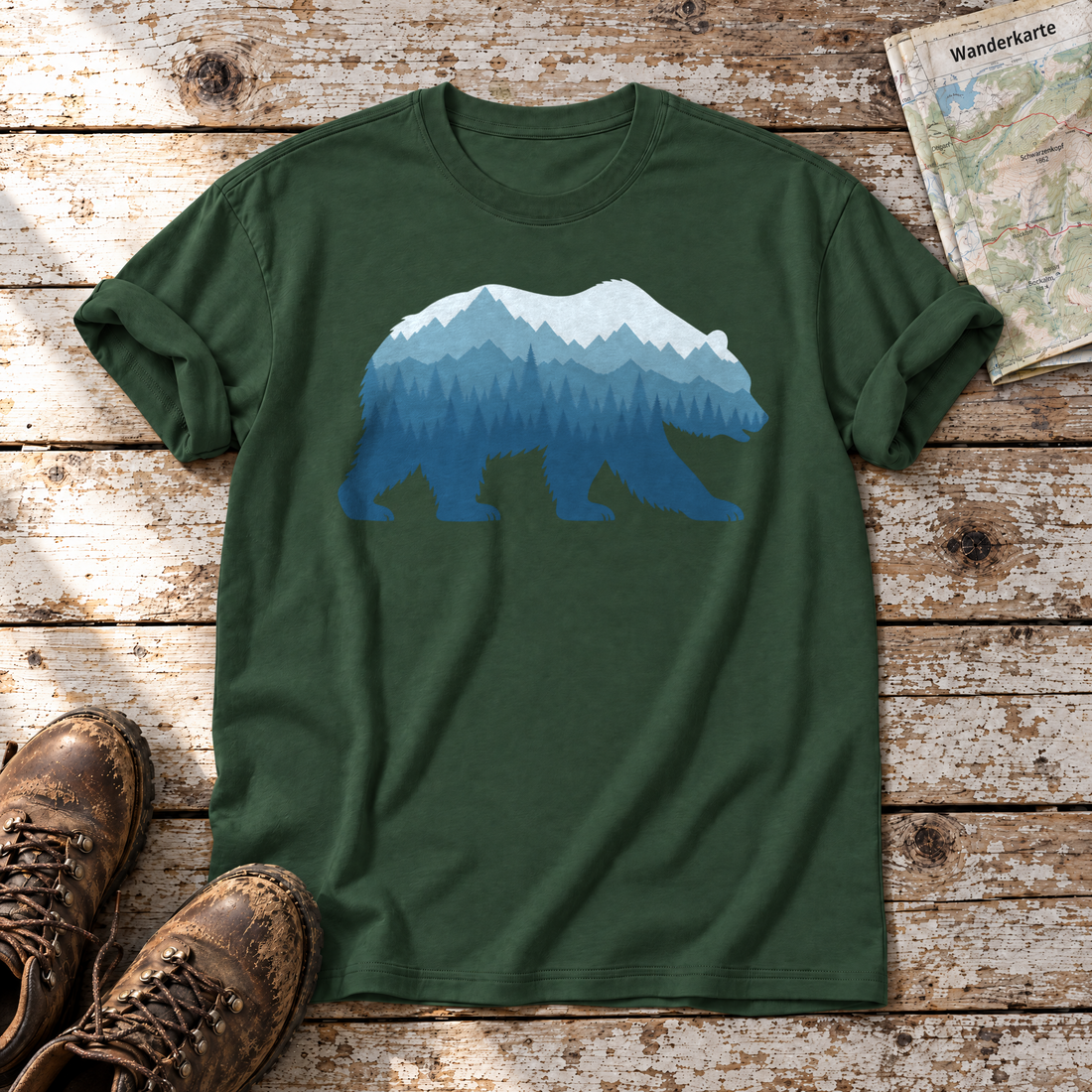Bär im Bergwald – T-Shirt Unisex in Flaschengrün, flach liegend auf alten Holzbrettern mit Wanderschuhen und Wanderkarte.