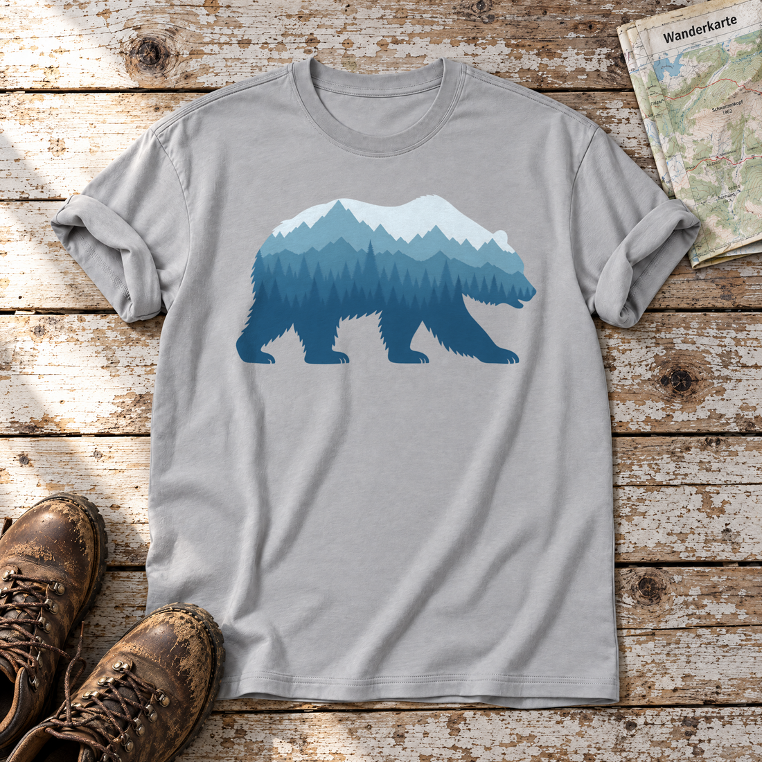 Bär im Bergwald – T-Shirt Unisex in Hellgrau, flach liegend auf alten Holzbrettern mit Wanderschuhen und Wanderkarte.
