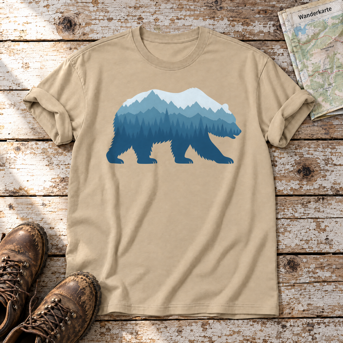 Bär im Bergwald – T-Shirt Unisex in Sand, flach liegend auf alten Holzbrettern mit Wanderschuhen und Wanderkarte.