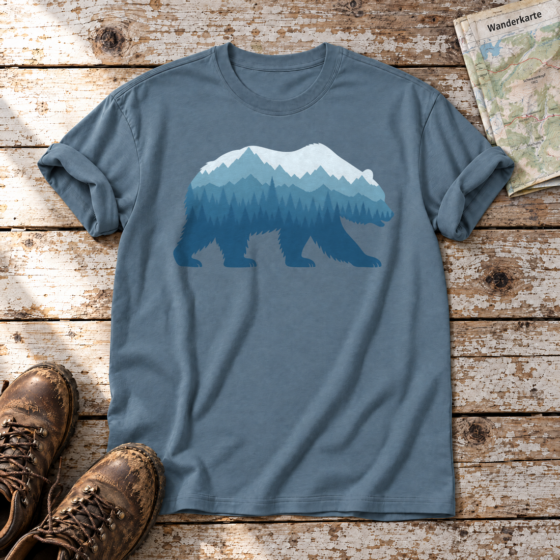 Bär im Bergwald – T-Shirt Unisex in Steinblau, flach liegend auf alten Holzbrettern mit Wanderschuhen und Wanderkarte.