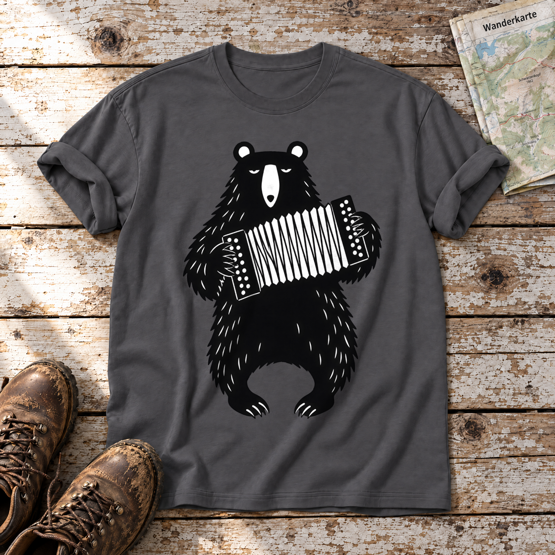 Bär mit Steirischer – T-Shirt Unisex in Dunkelgrau, flach liegend auf alten Holzbrettern mit Wanderschuhen und Wanderkarte.