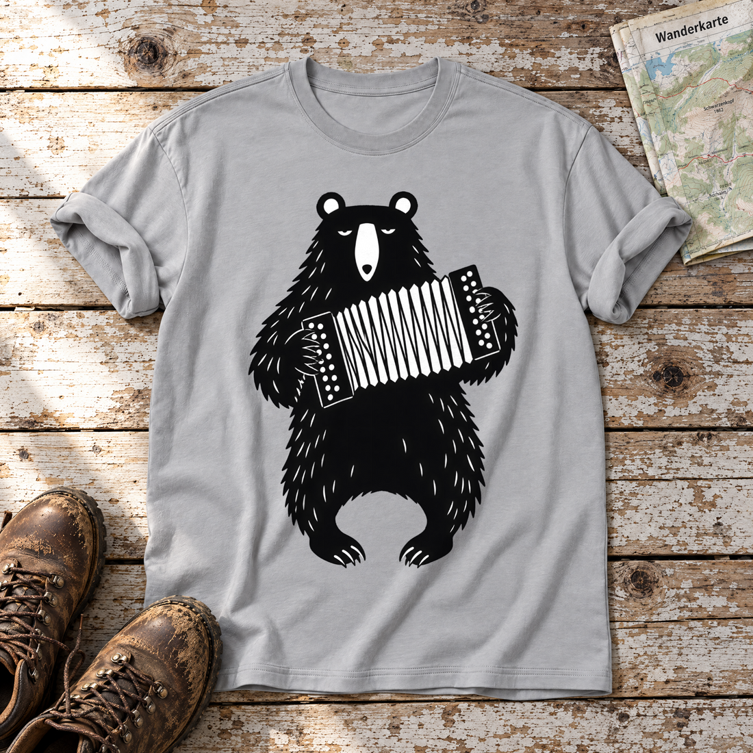 Bär mit Steirischer – T-Shirt Unisex in Hellgrau, flach liegend auf alten Holzbrettern mit Wanderschuhen und Wanderkarte.