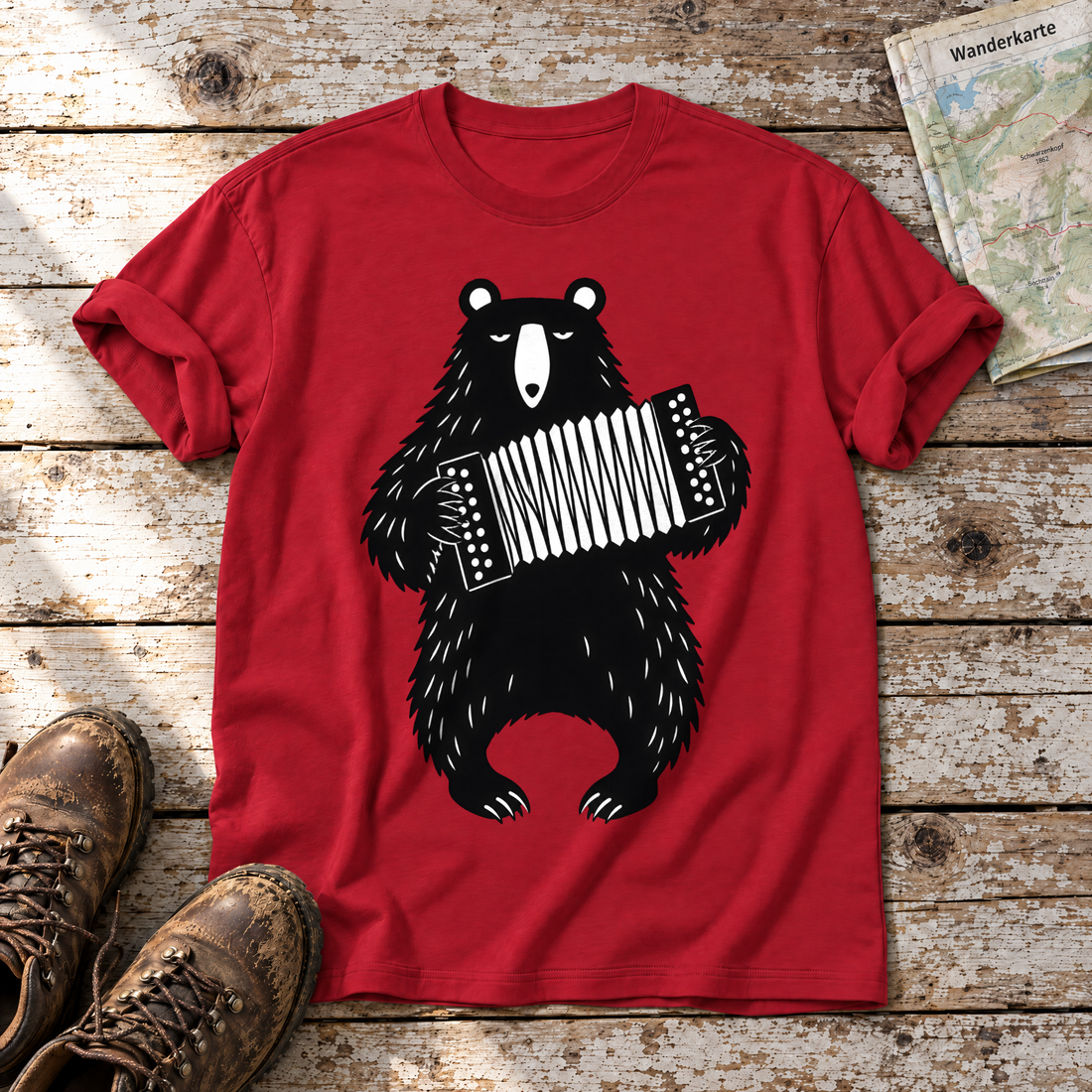 Bär mit Steirischer – T-Shirt Unisex in Rot, flach liegend auf alten Holzbrettern mit Wanderschuhen und Wanderkarte.