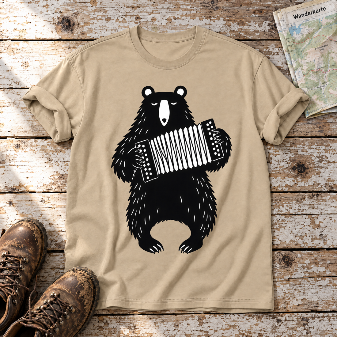 Bär mit Steirischer – T-Shirt Unisex in Sand, flach liegend auf alten Holzbrettern mit Wanderschuhen und Wanderkarte.