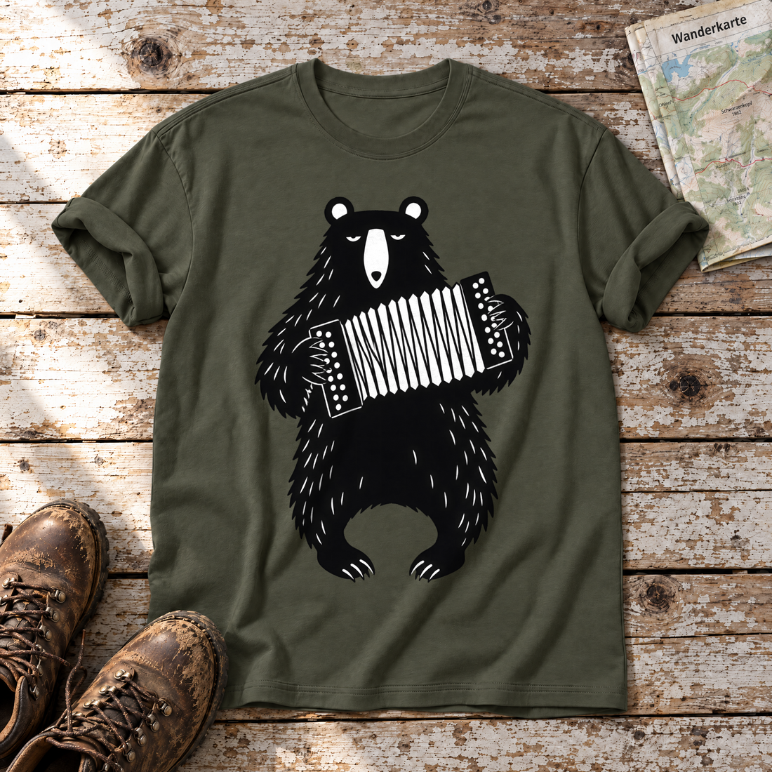 Bär mit Steirischer – T-Shirt Unisex in Oliv, flach liegend auf alten Holzbrettern mit Wanderschuhen und Wanderkarte.