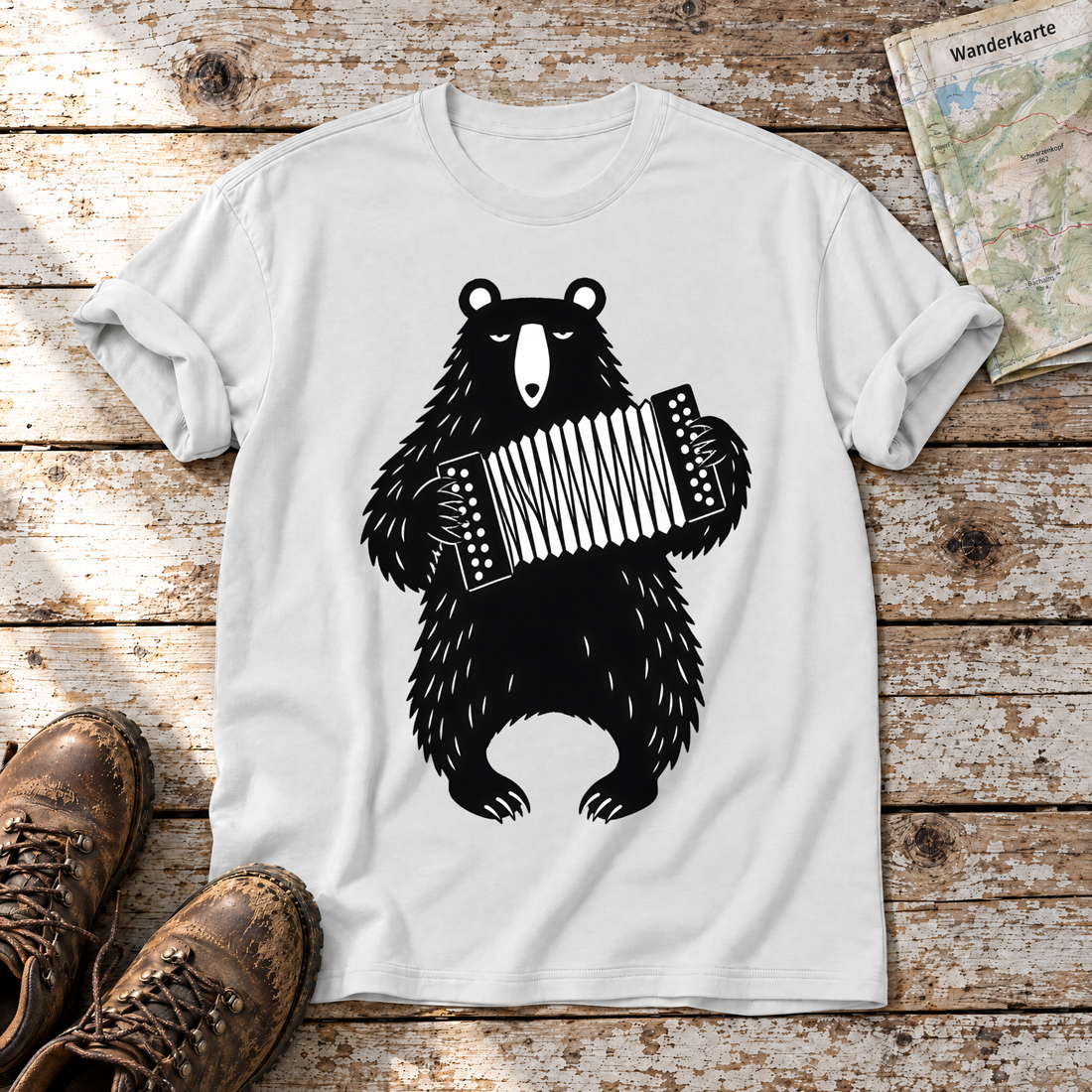 Bär mit Steirischer – T-Shirt Unisex in Weiß, flach liegend auf alten Holzbrettern mit Wanderschuhen und Wanderkarte.