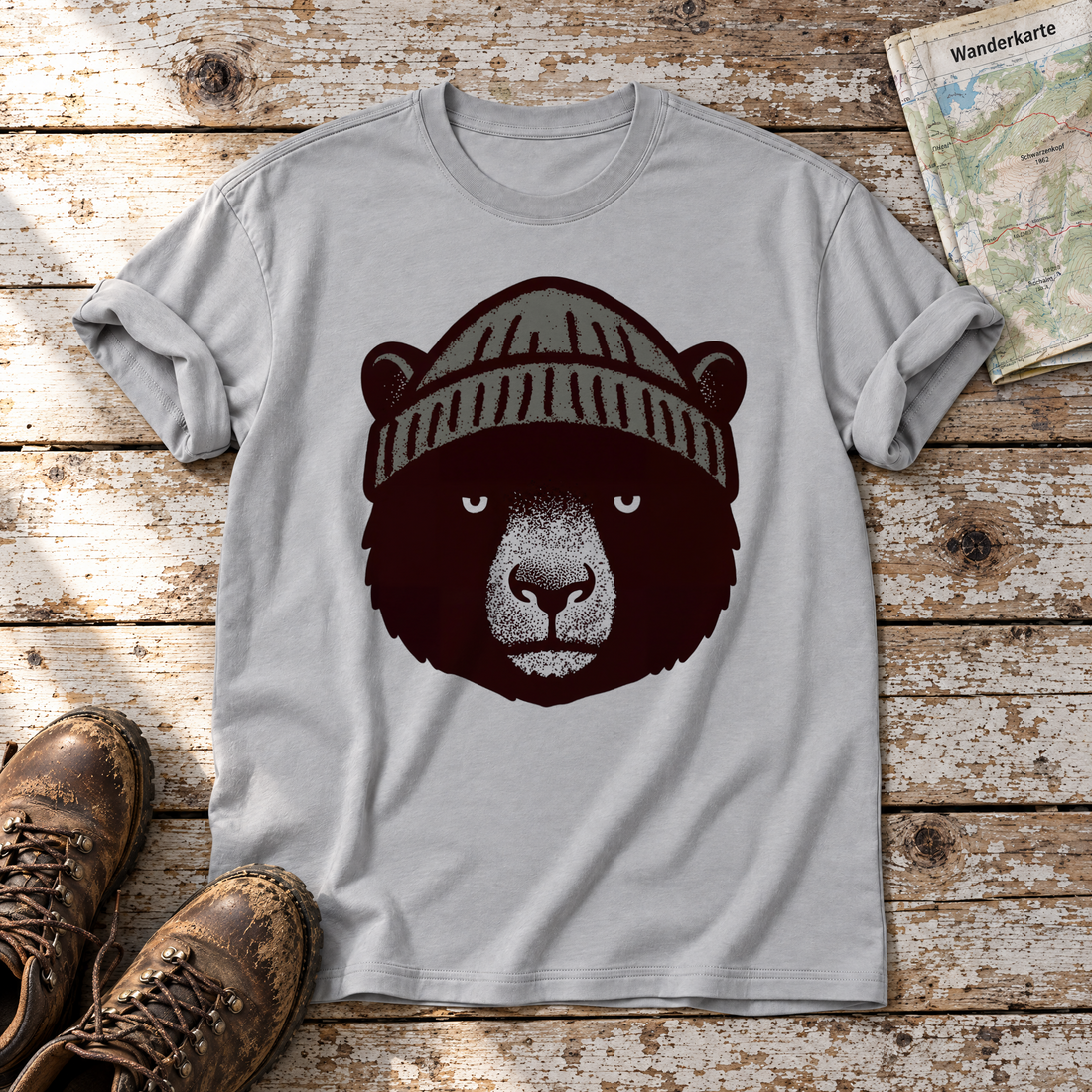 Bär mit Strickmütze – T-Shirt Unisex in Hellgrau, flach liegend auf alten Holzbrettern mit Wanderschuhen und Wanderkarte.