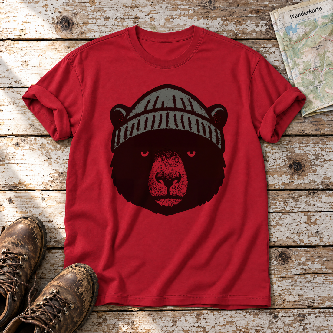 Bär mit Strickmütze – T-Shirt Unisex in Rot, flach liegend auf alten Holzbrettern mit Wanderschuhen und Wanderkarte.