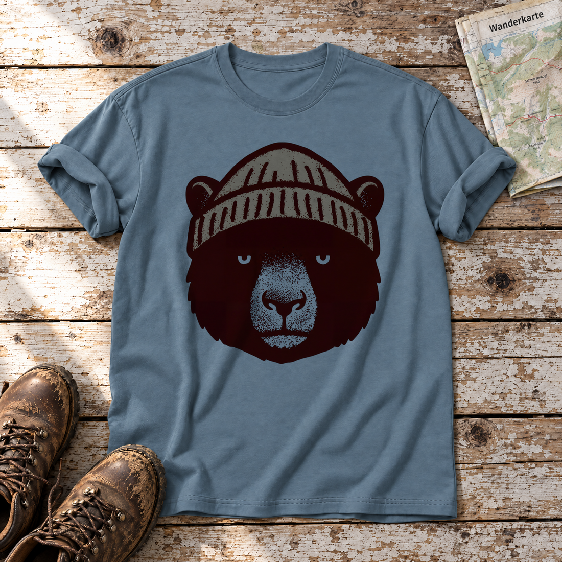 Bär mit Strickmütze – T-Shirt Unisex in Steinblau, flach liegend auf alten Holzbrettern mit Wanderschuhen und Wanderkarte.
