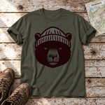 Bär mit Strickmütze – T-Shirt Unisex in Oliv, flach liegend auf alten Holzbrettern mit Wanderschuhen und Wanderkarte.