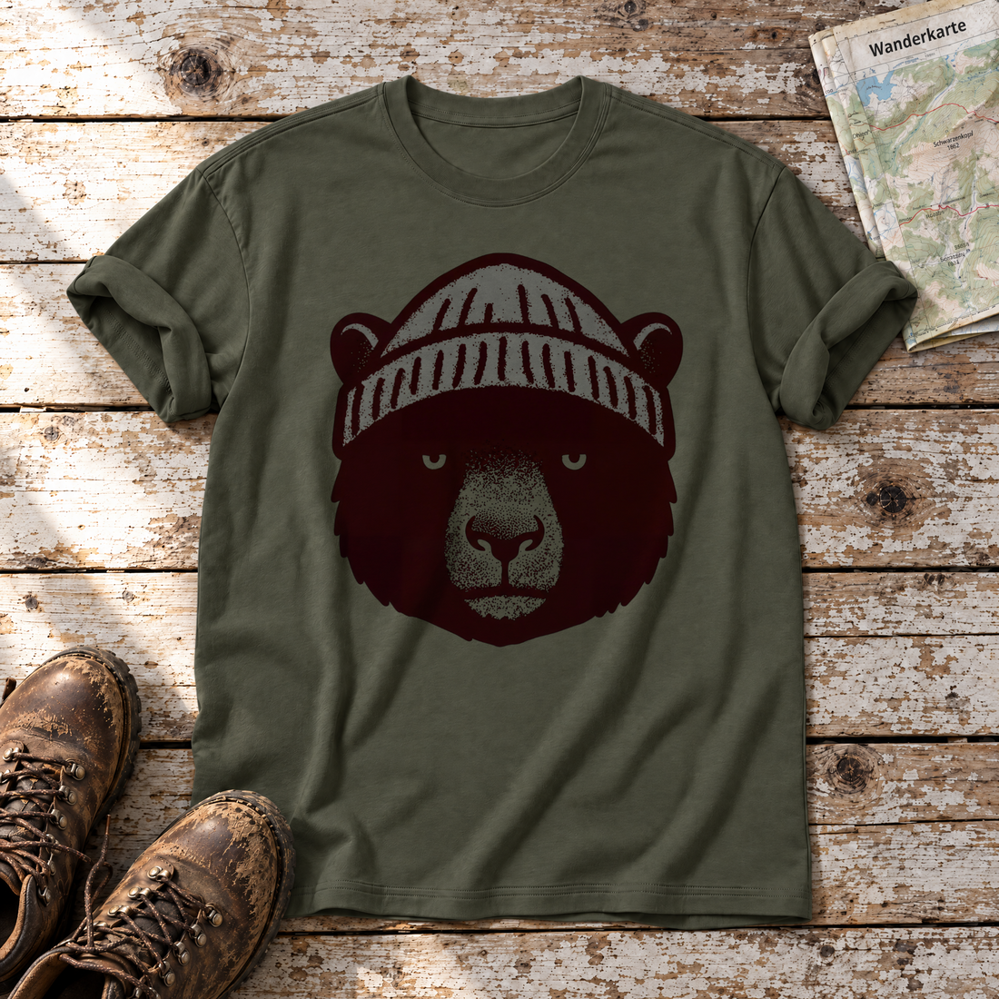 Bär mit Strickmütze – T-Shirt Unisex in Oliv, flach liegend auf alten Holzbrettern mit Wanderschuhen und Wanderkarte.