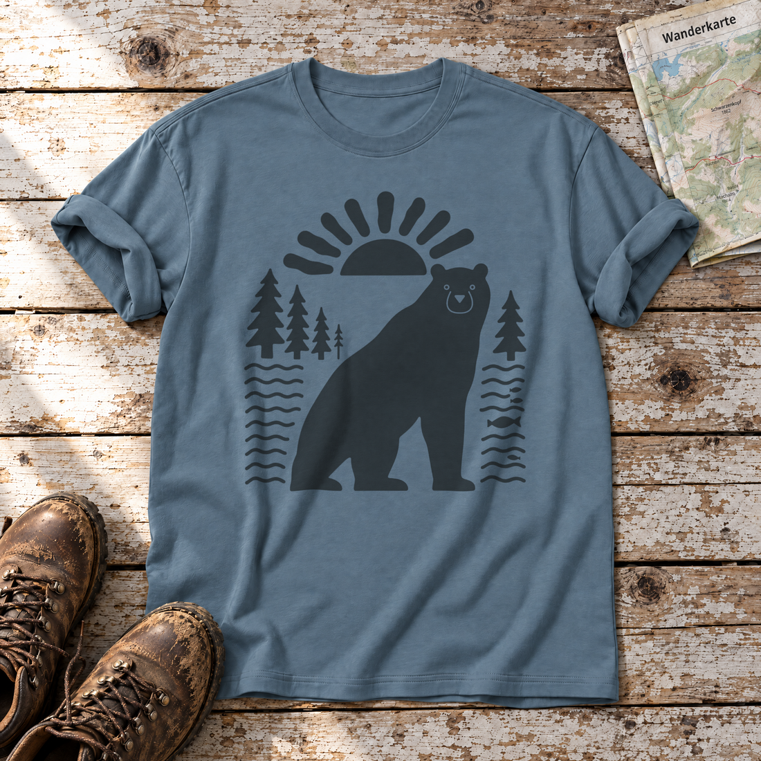 Bär im Sonnenbogen – T-Shirt Unisex in Steinblau, flach liegend auf alten Holzbrettern mit Wanderschuhen und Wanderkarte.