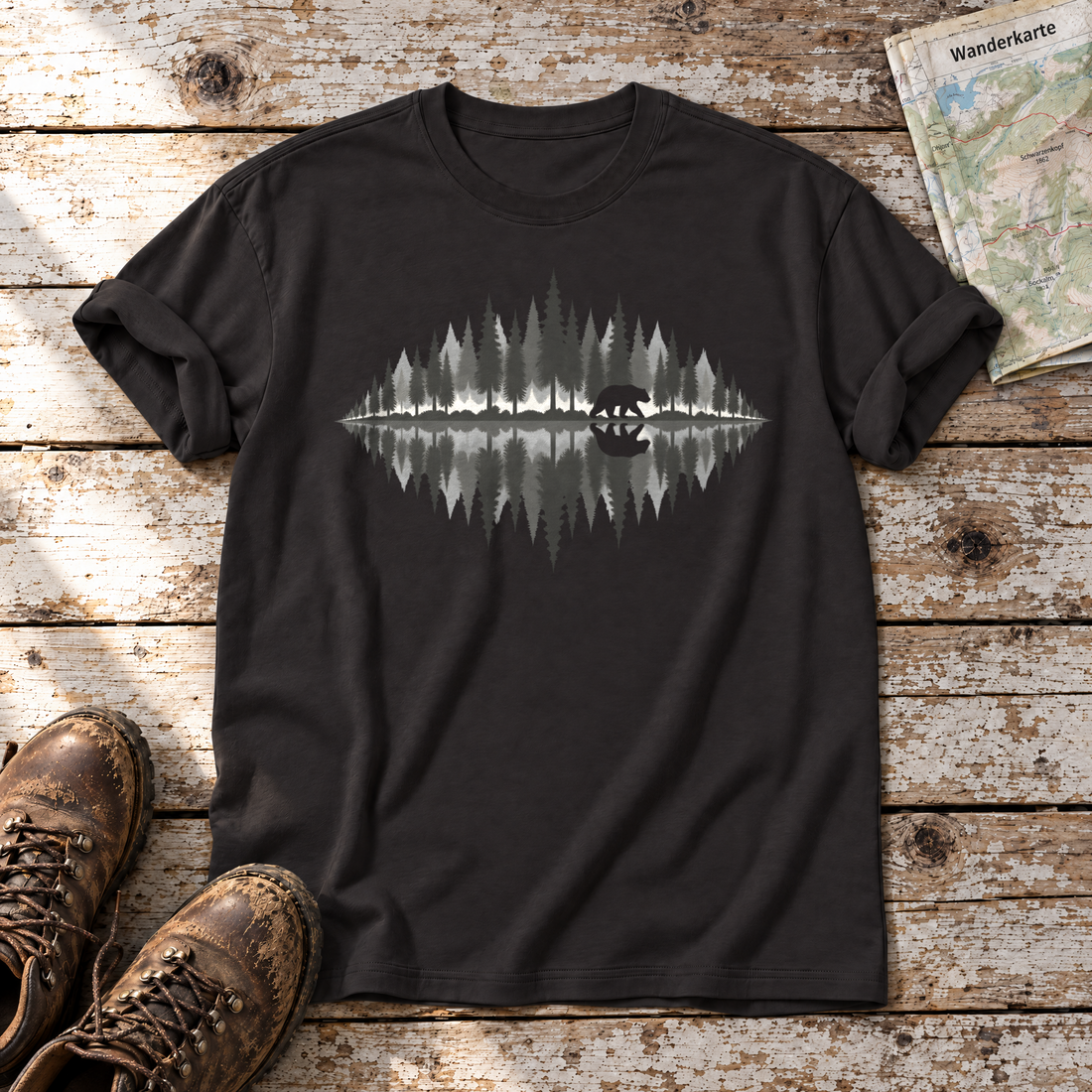 Bär am Waldsee – T-Shirt Unisex in Schwarz, flach liegend auf alten Holzbrettern mit Wanderschuhen und Wanderkarte.