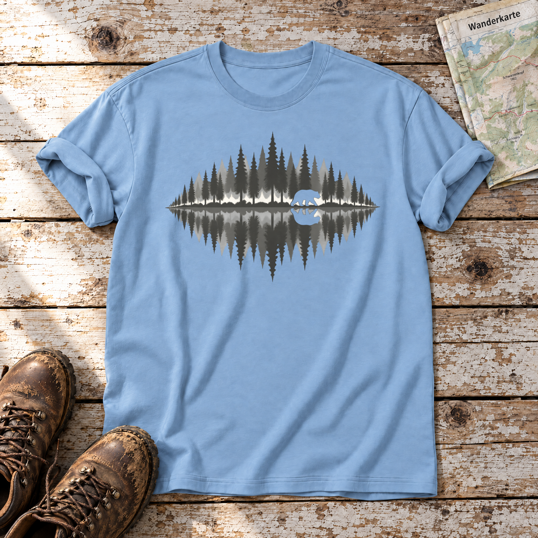 Bär am Waldsee – T-Shirt Unisex in Himmelblau, flach liegend auf alten Holzbrettern mit Wanderschuhen und Wanderkarte.