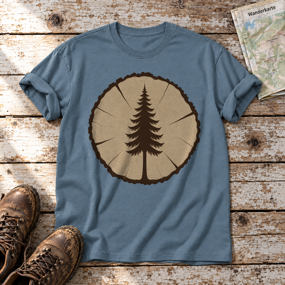 Fichte in der Baumscheibe – T-Shirt Unisex in Steinblau, flach liegend auf alten Holzbrettern mit Wanderschuhen und Wanderkarte.