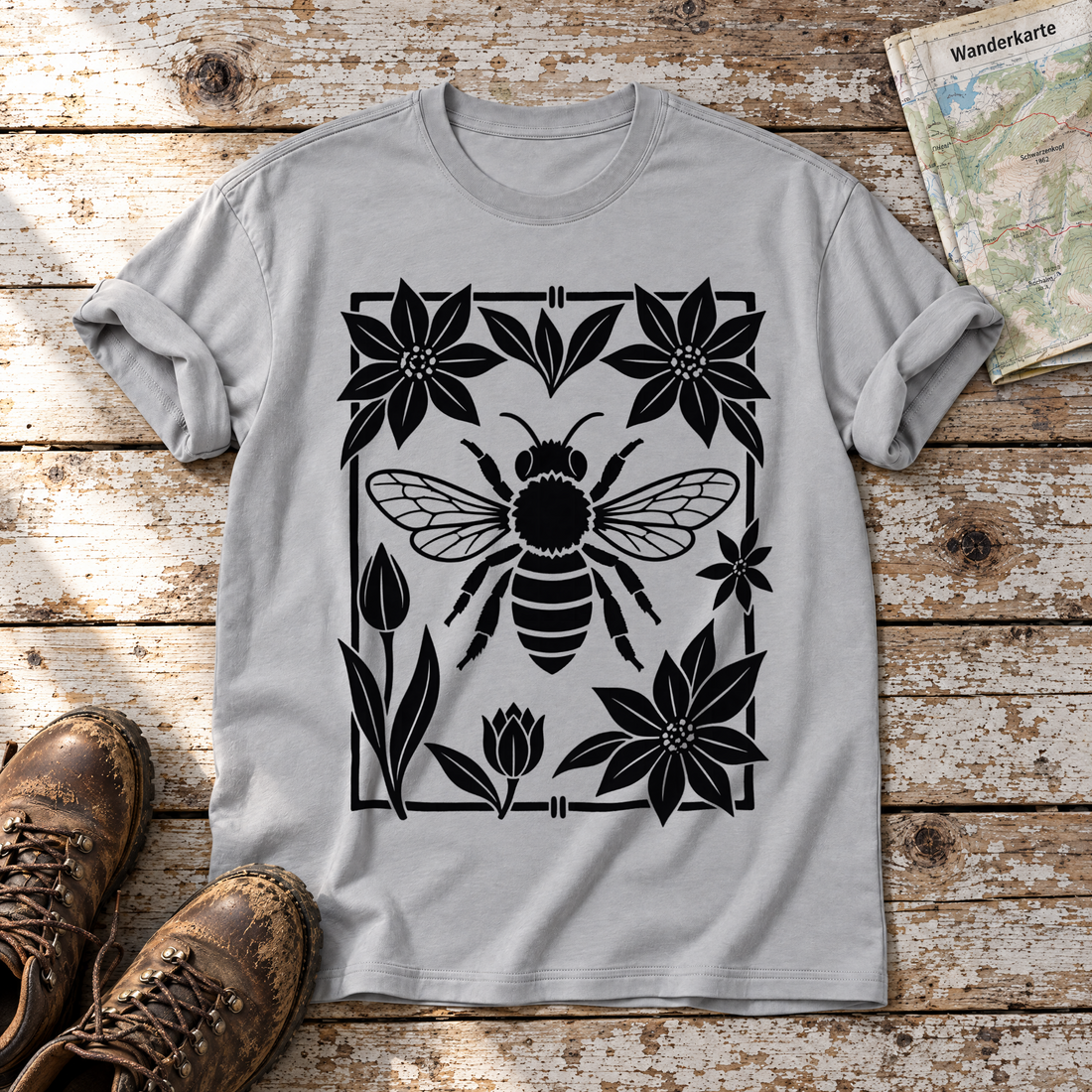 Biene im Blütenrahmen – T-Shirt Unisex in Hellgrau, flach liegend auf alten Holzbrettern mit Wanderschuhen und Wanderkarte.
