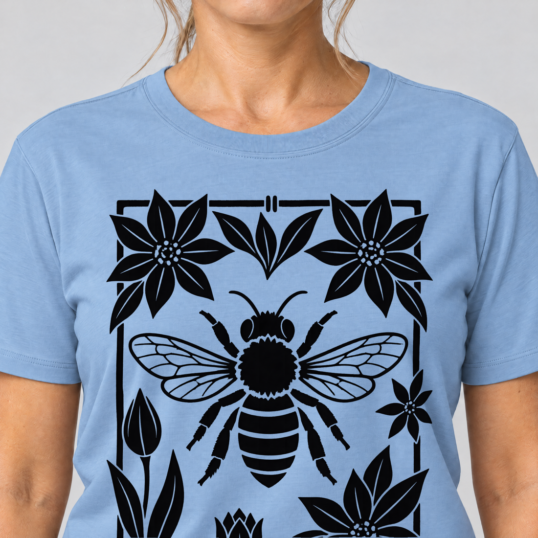 Nahaufnahme des Drucks: Biene im Blütenrahmen – T-Shirt Unisex in Himmelblau, von einer Frau getragen