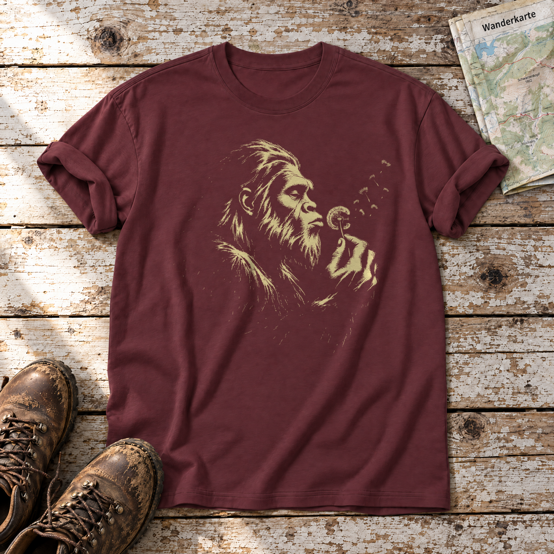 Bigfoot mit Pusteblume – T-Shirt Unisex in Bordeaux, flach liegend auf alten Holzbrettern mit Wanderschuhen und Wanderkarte.