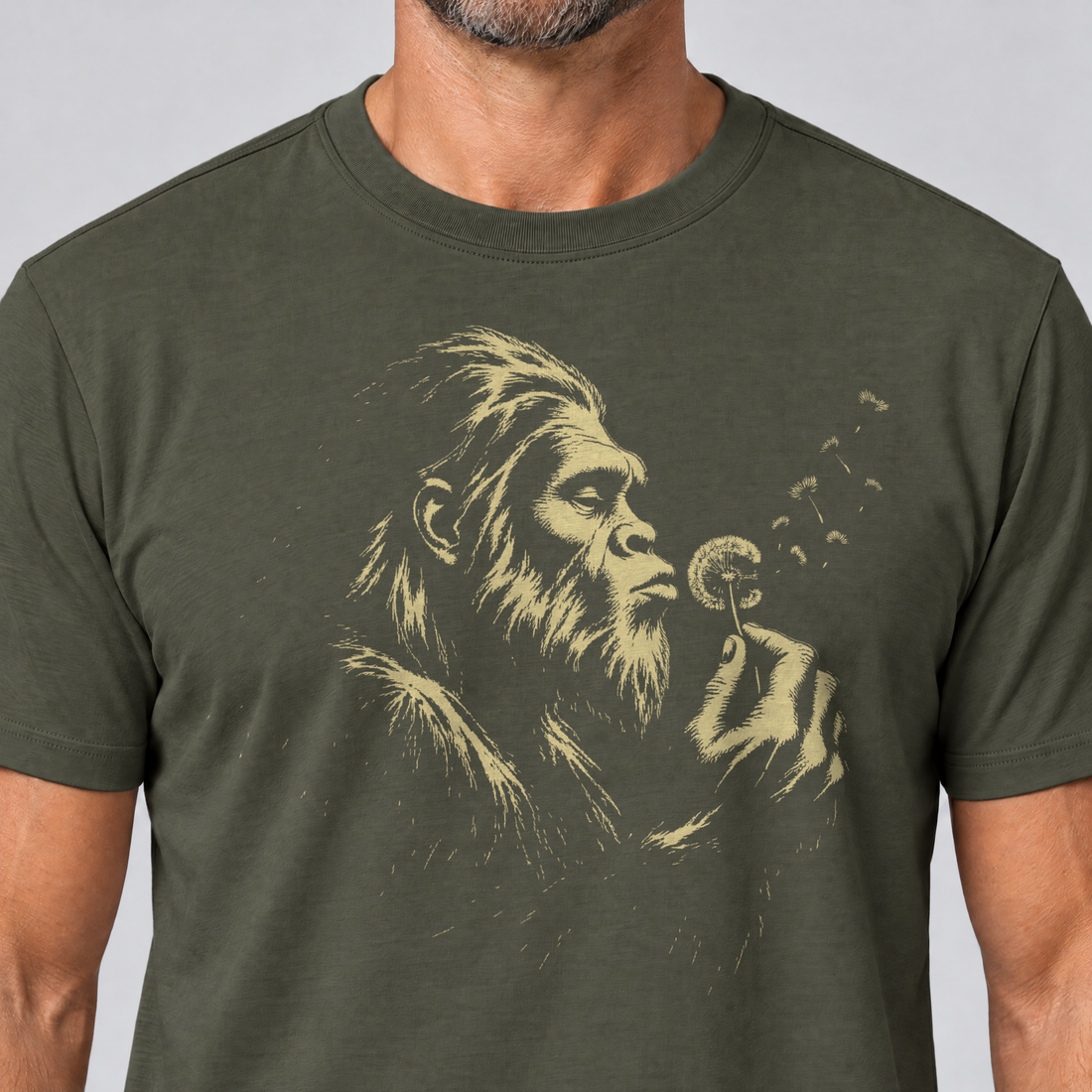 Nahaufnahme des Drucks: Bigfoot mit Pusteblume – T-Shirt Unisex in Oliv, von einem Mann getragen