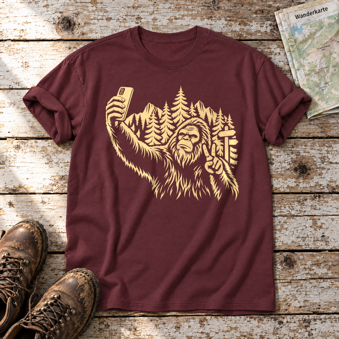 Bigfoot-Selfie im Bergwald – T-Shirt Unisex in Bordeaux, flach liegend auf alten Holzbrettern mit Wanderschuhen und Wanderkarte.