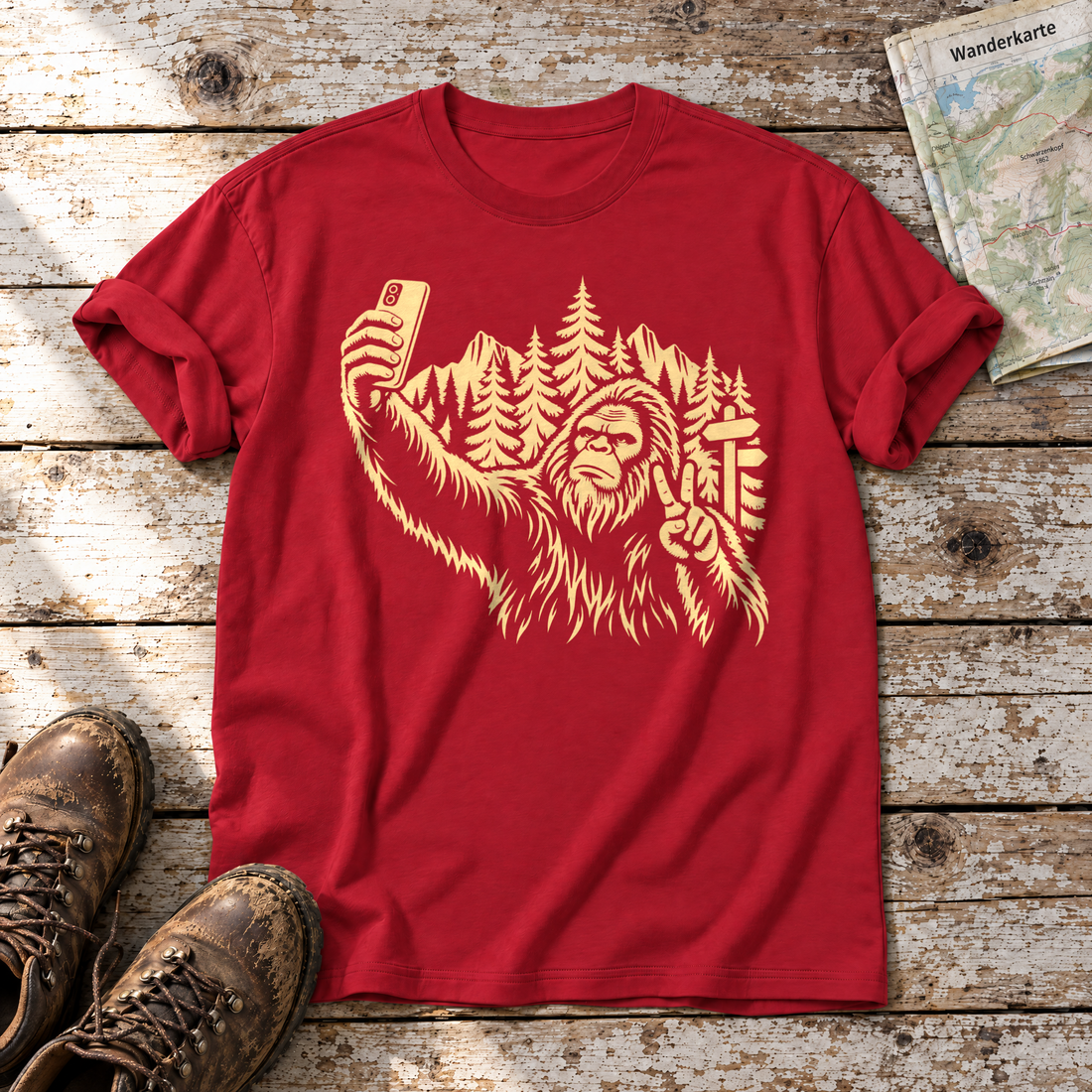 Bigfoot-Selfie im Bergwald – T-Shirt Unisex in Rot, flach liegend auf alten Holzbrettern mit Wanderschuhen und Wanderkarte.