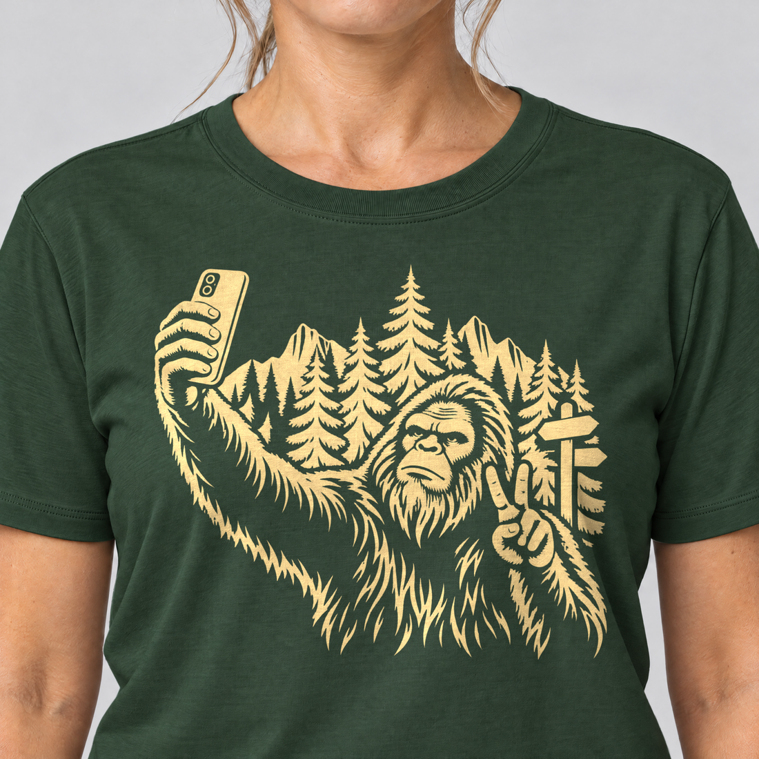 Nahaufnahme des Drucks: Bigfoot-Selfie im Bergwald – T-Shirt Unisex in Flaschengrün, von einer Frau getragen