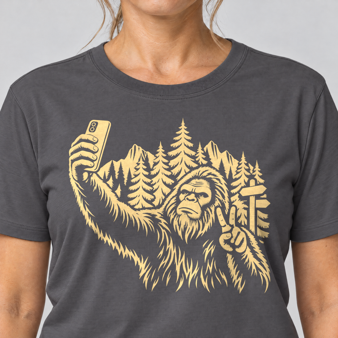 Nahaufnahme des Drucks: Bigfoot-Selfie im Bergwald – T-Shirt Unisex in Dunkelgrau, von einer Frau getragen