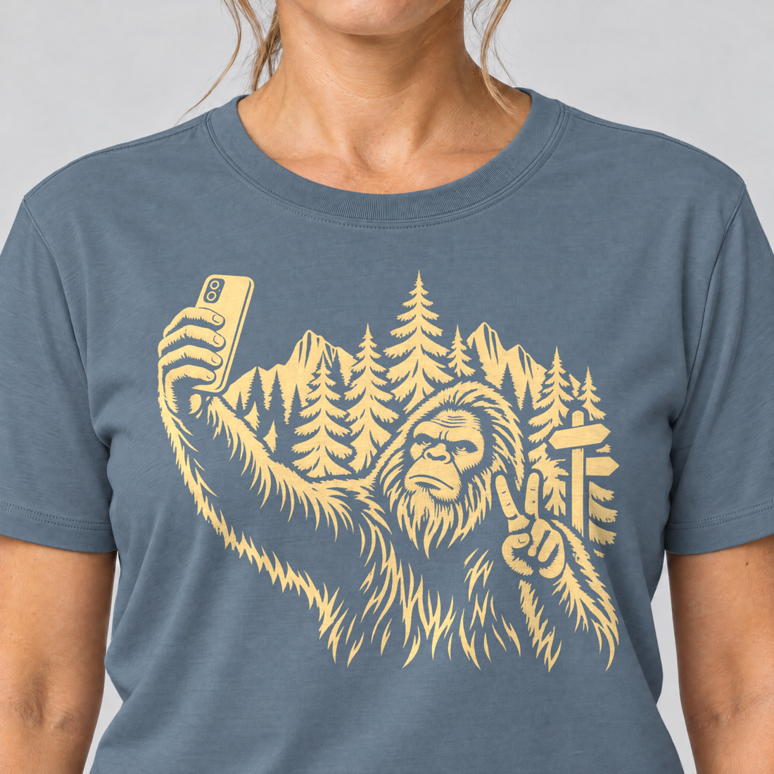Nahaufnahme des Drucks: Bigfoot-Selfie im Bergwald – T-Shirt Unisex in Steinblau, von einer Frau getragen
