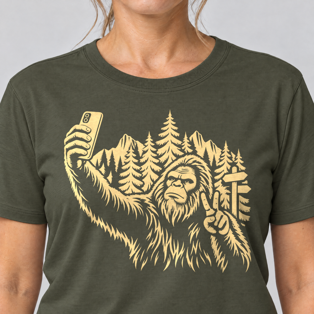Nahaufnahme des Drucks: Bigfoot-Selfie im Bergwald – T-Shirt Unisex in Oliv, von einer Frau getragen