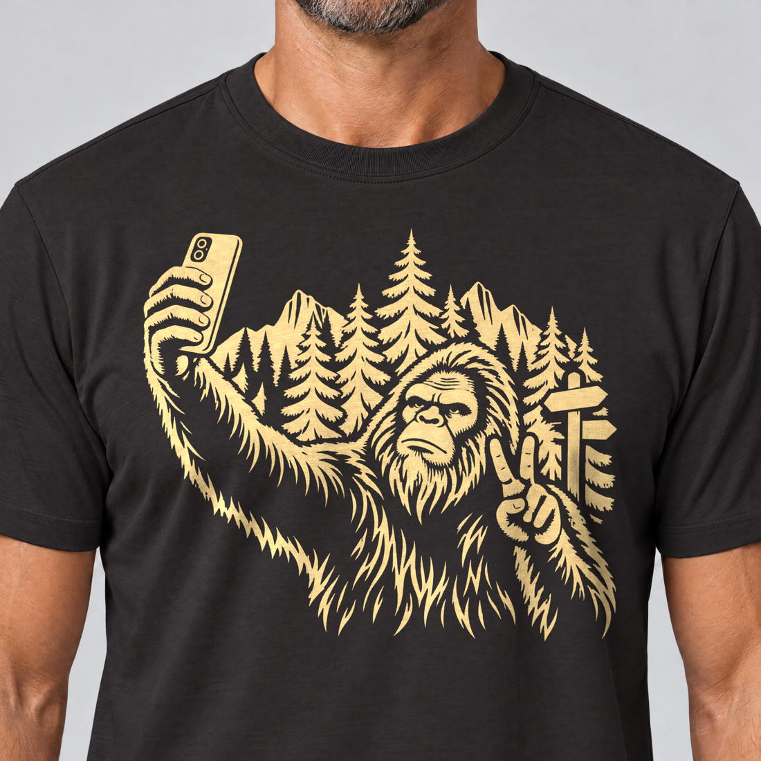 Nahaufnahme des Drucks: Bigfoot-Selfie im Bergwald – T-Shirt Unisex in Schwarz, von einem Mann getragen