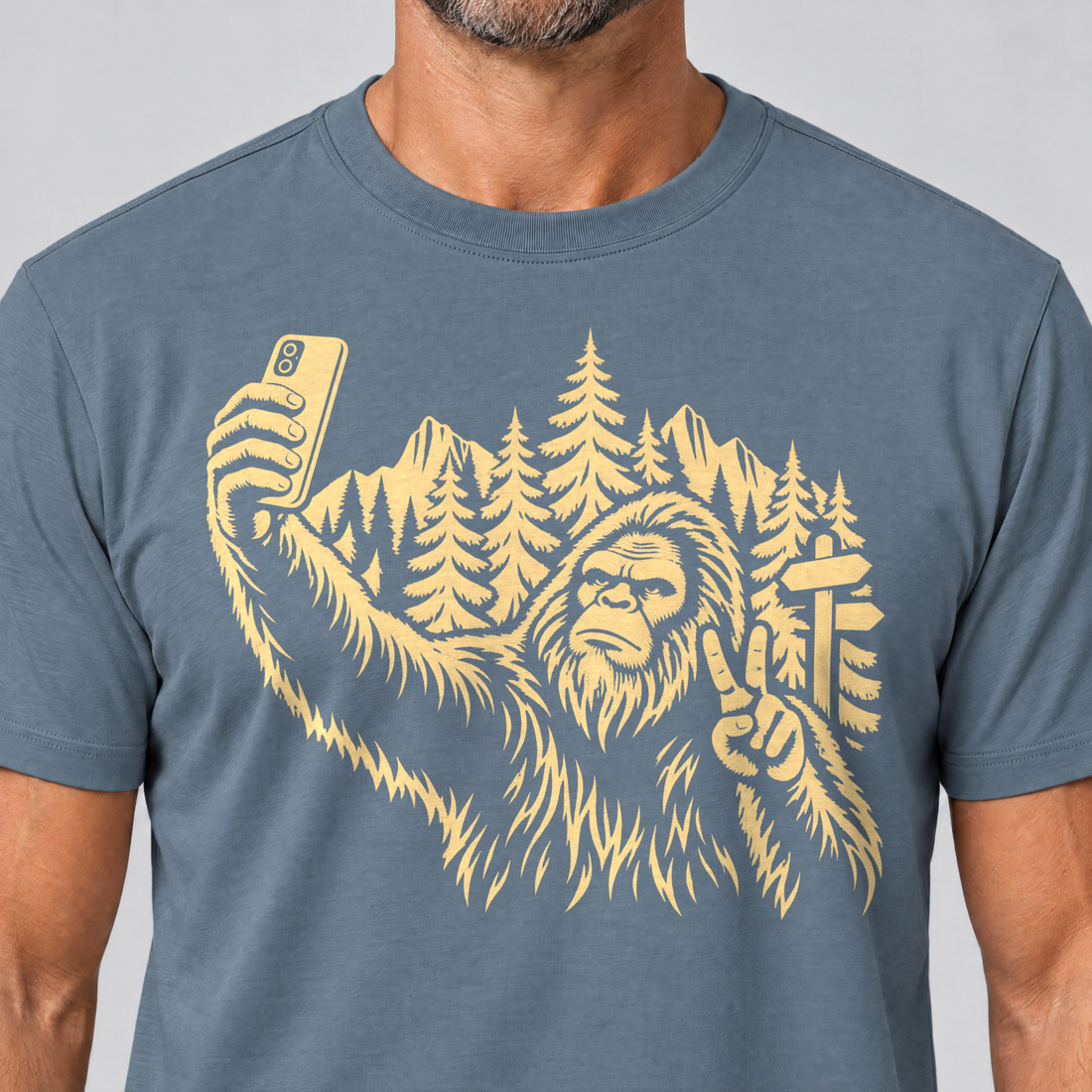 Nahaufnahme des Drucks: Bigfoot-Selfie im Bergwald – T-Shirt Unisex in Steinblau, von einem Mann getragen