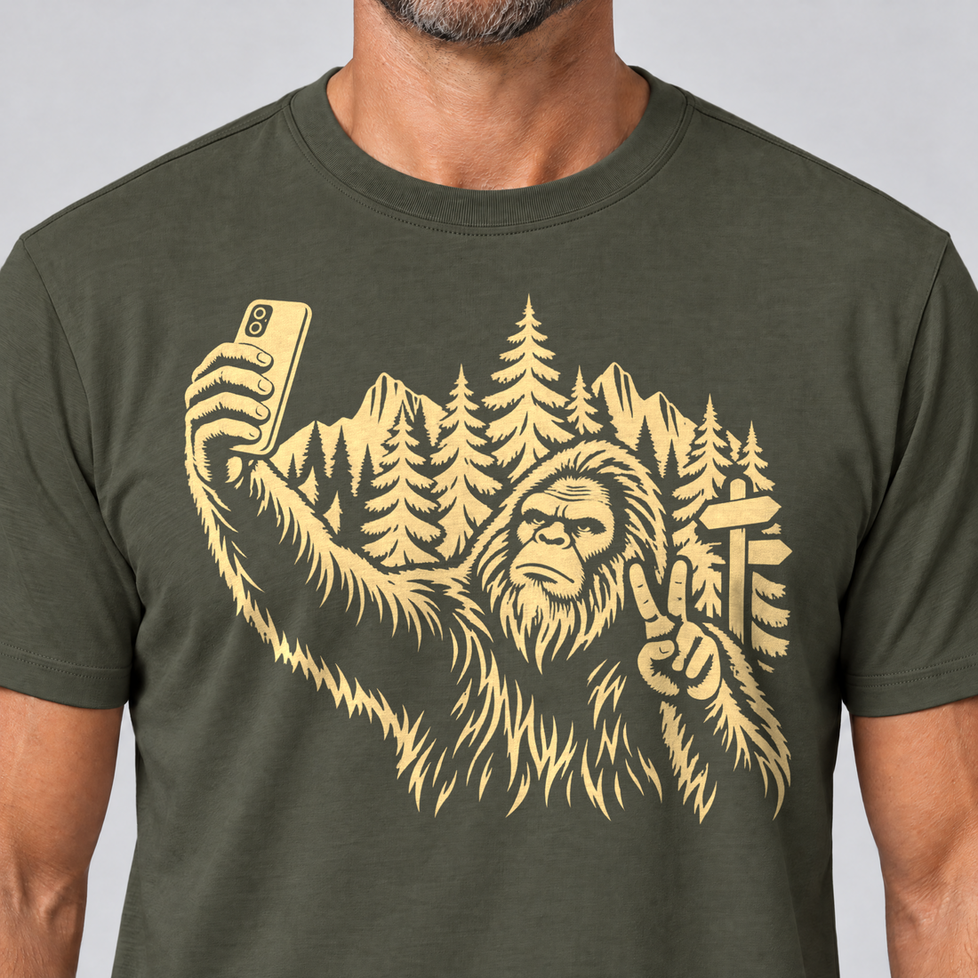 Nahaufnahme des Drucks: Bigfoot-Selfie im Bergwald – T-Shirt Unisex in Oliv, von einem Mann getragen