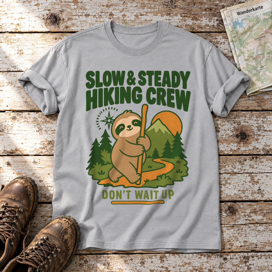 Slow & Steady Hiking Crew – T-Shirt Unisex in Hellgrau, flach liegend auf alten Holzbrettern mit Wanderschuhen und Wanderkarte.