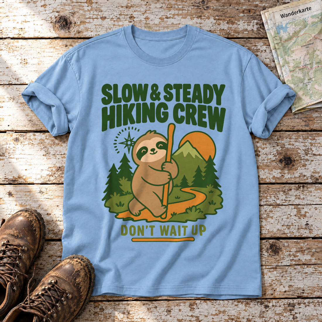 Slow & Steady Hiking Crew – T-Shirt Unisex in Himmelblau, flach liegend auf alten Holzbrettern mit Wanderschuhen und Wanderkarte.