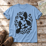 Elsternpaar im Scherenschnitt – T-Shirt Unisex in Himmelblau, flach liegend auf alten Holzbrettern mit Wanderschuhen und Wanderkarte.